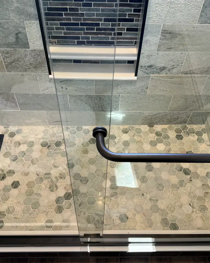 A tiled shower floor with a teak bench and a glass door