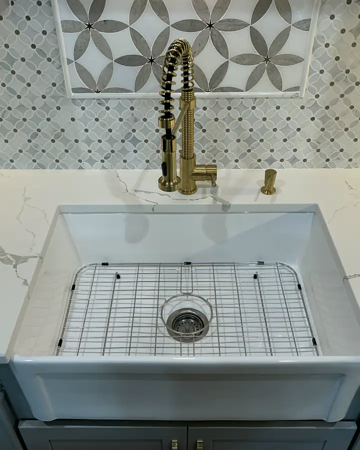 A farmhouse sink with a brass faucet and a patterned tile backsplash